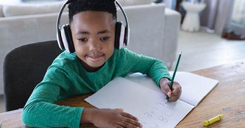 A student wearing a green shirt sitting at the table working on an assignment for Connections Academy.